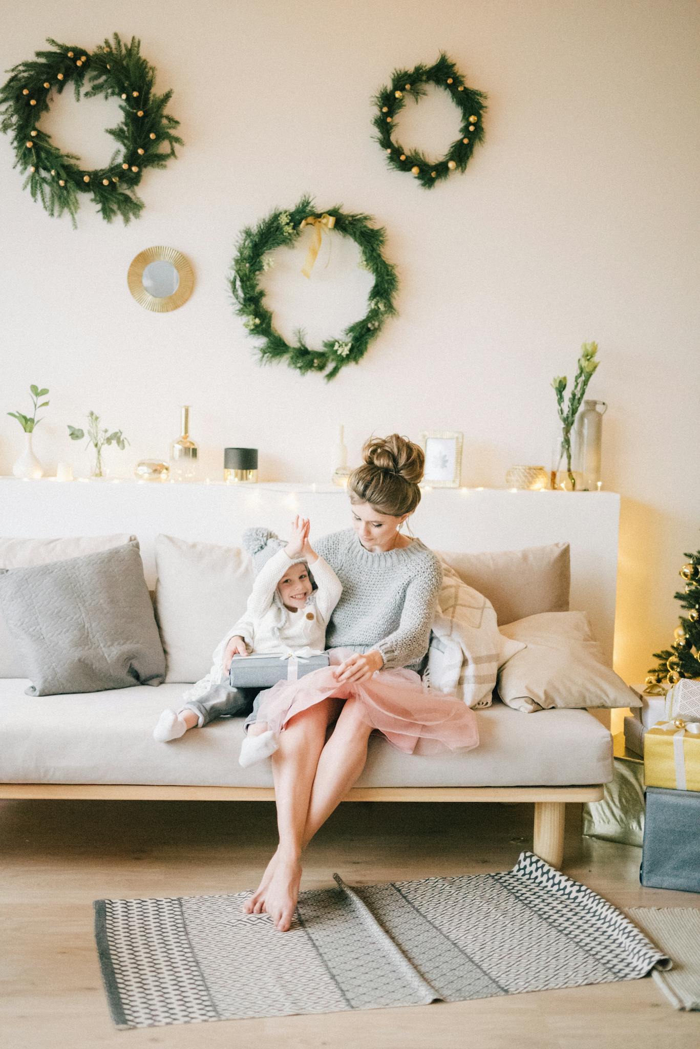 A mother and daughter sitting on a sofa, enjoying Christmas decorations indoors.