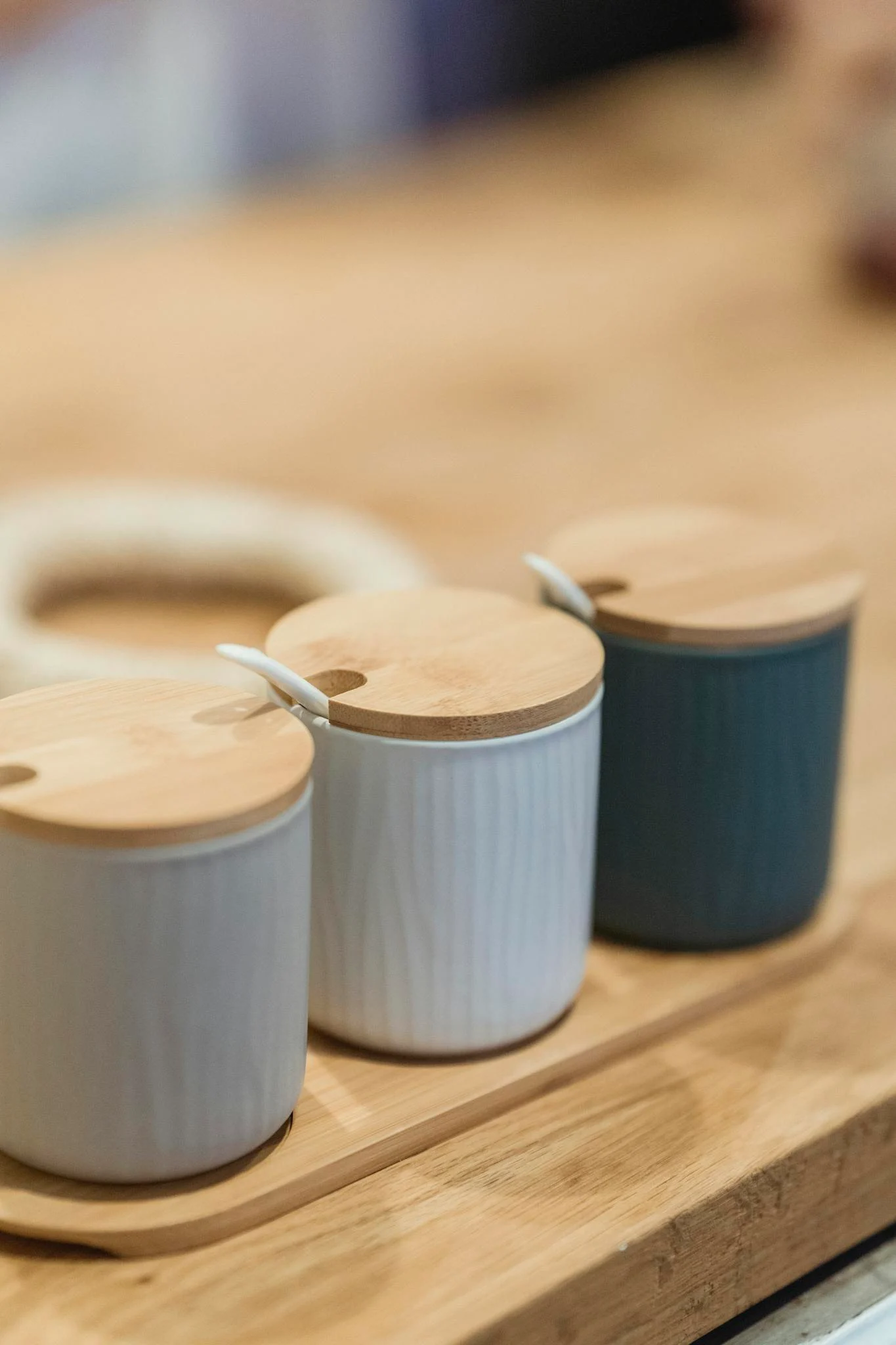 Three ceramic pots with wooden lids on a wooden tray, perfect for kitchen seasoning storage.